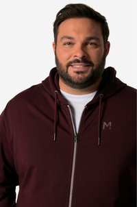 Burgundy zip-up hoodie with drawstrings, featuring a textured fabric, a subtle logo, and a white T-shirt underneath.