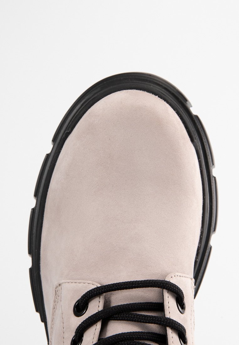 Zapato de ante gris claro con puntera redonda, suela de goma negra y cordones negros; cuenta con una textura lisa y un diseño minimalista.