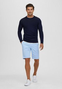Marineblauwe gebreide trui met een witte kraagdetail, gecombineerd met lichtblauwe short. De outfit wordt aangevuld met witte sneakers.