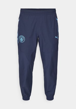 Navy athletic pants with an elastic waistband, tapered cuffs, light blue accents, and Manchester City crest on the left thigh.