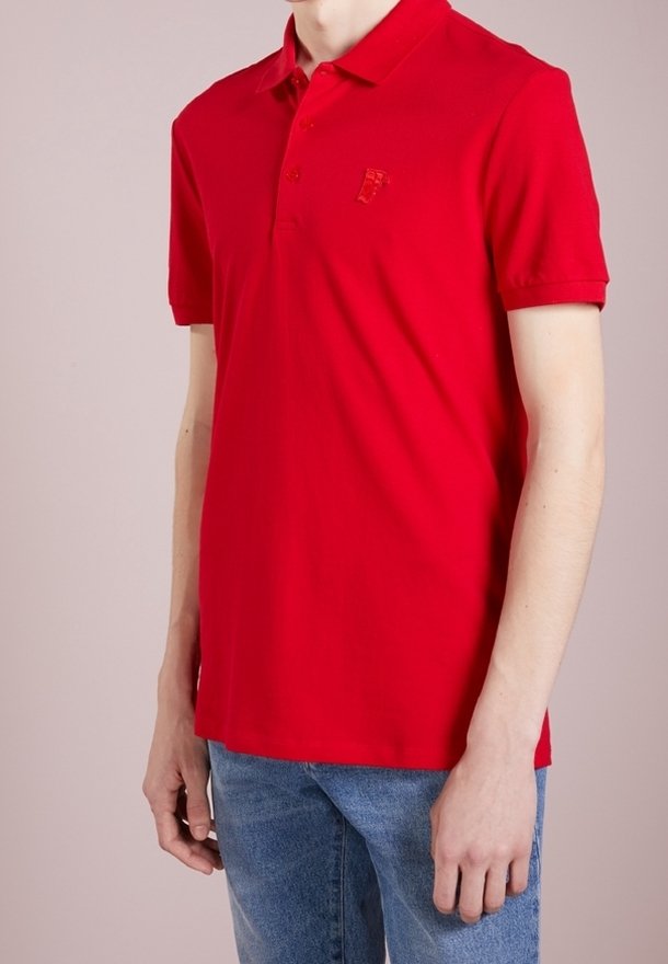 Polo rouge en coton, avec un col, des manches courtes et un petit logo sur la poitrine. Associé à un jean denim bleu clair.