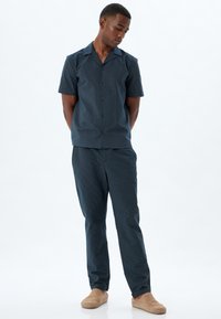 Mörkblå kortärmad skjorta med knappar och ett strukturerat mönster, ihopparad med matchande byxor. Mjuk tyg, avslappnad passform och ljusa skor.