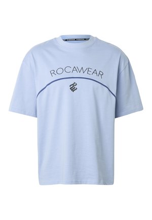 Világoskék rövid ujjú póló, amelyen a "ROCAWEAR" felirat ívelt formában látható egy sötétkék, ívelt vonal felett, alatta pedig egy fekete, stilizált "RW" logó.