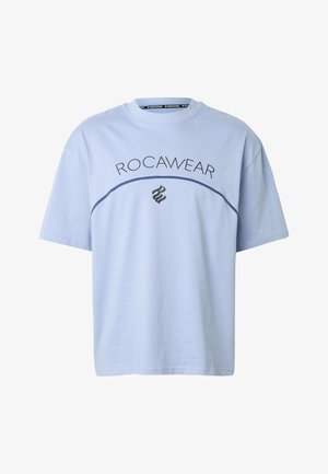 Világoskék rövid ujjú póló, amelyen a "ROCAWEAR" felirat ívelt formában látható egy sötétkék, ívelt vonal felett, alatta pedig egy fekete, stilizált "RW" logó.