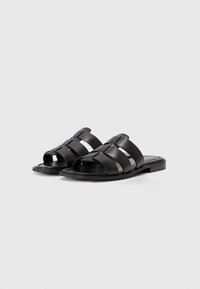 Black leather slide sandals with a wide strap design featuring horizontal cutouts, a flat sole, and a smooth finish.