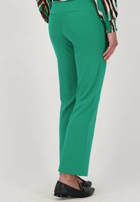 Groene stretchbroek met een slim fit, met een gladde textuur en twee achterzakken. Gemaakt in combinatie met platte zwarte schoenen.