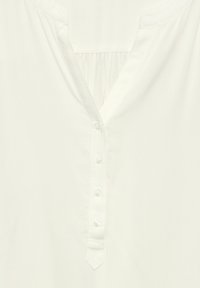 Blouse blanche avec un décolleté en V, patte de boutonnage et un dos plissé. Texture lisse avec un léger éclat, manches courtes et coupe ajustée.