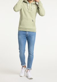 Felpa verde chiaro con tasca a canguro, cappuccio con cordino e piccolo logo. Abbinata a jeans slim blu chiaro e sneakers bianche.