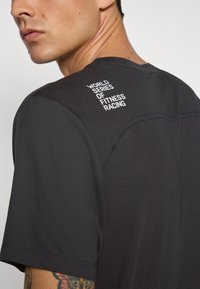 Sort atletisk t-shirt med korte ærmer, prydet med et hvidt trykt logo "WORLD SERIES OF FITNESS RACING" på den øvre ryg, og glat tekstur.