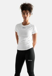 Witte sportieve T-shirt met korte mouwen en logo op de borst, gecombineerd met aansluitende zwarte leggings met logo aan de zijkant. Glad materiaal.