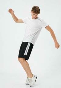 Hvid atletisk t-shirt med grå accenter, parret med sorte shorts med sidetekst og en afslappet pasform. Sneakers i neutrale nuancer fuldender looket.