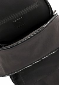 Must nahast kott hõbedase tõmblukuga, mis on osaliselt avatud, paljastades sisemise tõmblukuga tasku ja õmmeldud brändilogo plaastri.