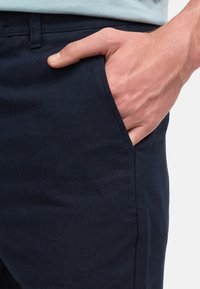 Pantaloni blu navy in cotone, dotati di una tasca laterale e una superficie liscia, con una cucitura visibile lungo la gamba.