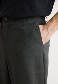 Pantalons à carreaux gris avec une silhouette ajustée, dotés d'une poche latérale et d'un tissu légèrement texturé. Fermeture standard par bouton.