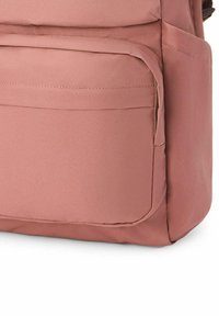 Primer plano frontal de un bolsillo de mochila rosa polvoriento con costuras visibles y refuerzos en las uniones del material de tela.