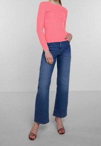Rosa geripptes Langarmoberteil kombiniert mit blauen weit geschnittenen Jeans. Das Model trägt braune Riemchen-Heels. Glatte Textur, figurbetontes Design und lebendige Farbe.