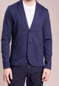 Námořnický modrý blejzr z jemného úpletu, s klopovým límcem, jednobuttonovým zapínáním, dvěma předními kapsami a přiléhavým střihem.