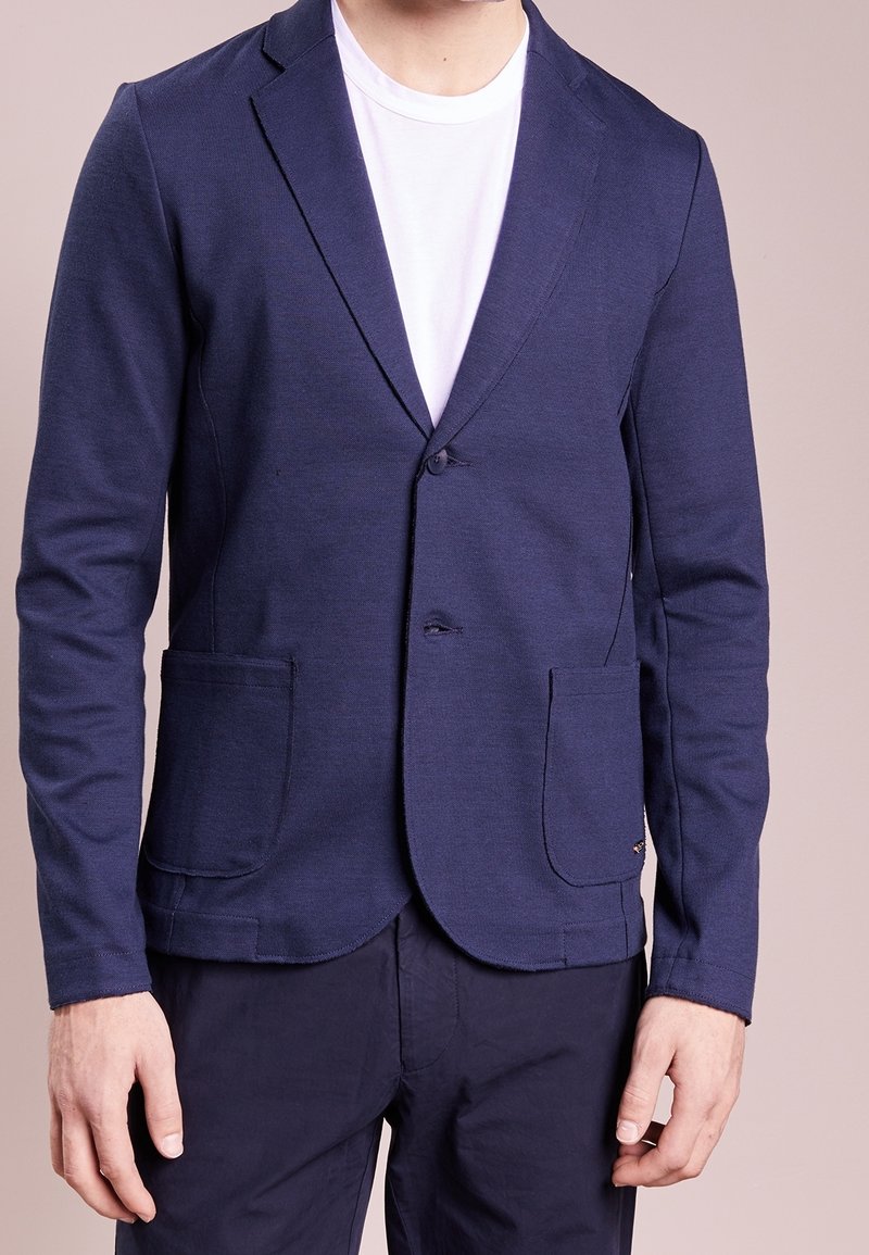 Námořnický modrý blejzr z jemného úpletu, s klopovým límcem, jednobuttonovým zapínáním, dvěma předními kapsami a přiléhavým střihem.