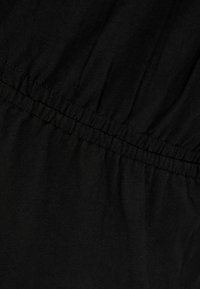 Musta kangas, jossa on sileä rakenne, varustettu joustavalla kerroksellisella vyötäröllä. Hienovaraisten ryppyjen mukana tulee ulkomuotoon syvyys.