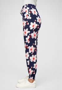 Pantaloni floreali blu navy con grandi fantasie di fiori bianchi e rosa. Vita elastica, vestibilità rilassata, polsini arricciati, abbinati a sneaker bianche.