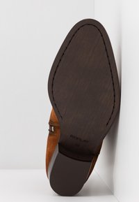 Suela de zapato de ante marrón con un fondo liso, similar a la madera oscura, con marcas de la marca y costuras detalladas a lo largo de los bordes.