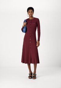 Burgundy csíkozott midi ruha hosszú ujjakkal, elülső gombos záródással, két zsebel a mellrészen és bővülő szoknyával. Kék táskával párosítva.