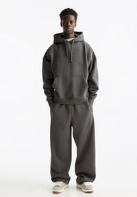 Grijze oversized hoodie met een voorzak en trekkoord, gecombineerd met bijpassende losse sweatpants. Beide zijn gemaakt van zachte, gestructureerde stof.
