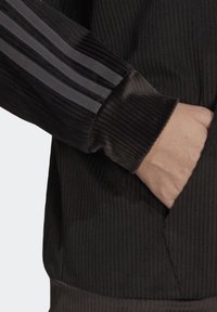 Svart ribbad jacka med mjuk textur, med grå randiga detaljer på ärmarna och en framficka.