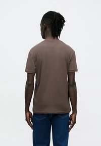 Bruin katoenen T-shirt met korte mouwen, een ronde hals en een rechte zoom. Draagt blauwe spijkerbroek, toont een eenvoudig ontwerp.