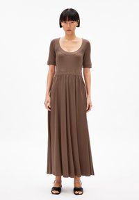 Brown, knee-length dress with short sleeves, scoop neckline, and gathered waist. Smooth, lightweight fabric flows to the ankle. Black heeled sandals.