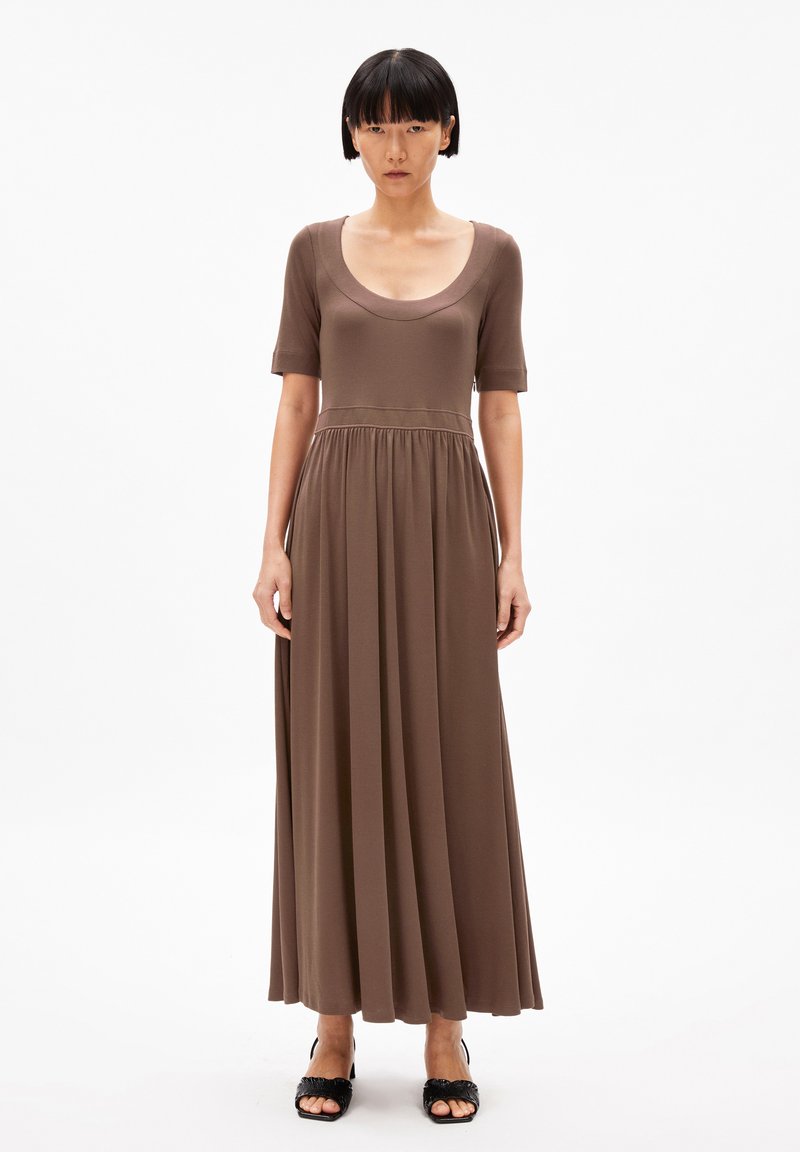 Brown, knee-length dress with short sleeves, scoop neckline, and gathered waist. Smooth, lightweight fabric flows to the ankle. Black heeled sandals.