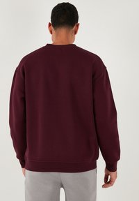 Bordeaux sweatshirt met een ronde halslijn en verlaagde schoudernaden. Gemaakt van zachte stof, met ribgebreide boorden en zoom.