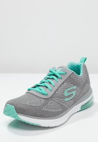 Grå och teal träningssko med meshtyg, teal snören, mönstrad inredning och transparent luftkudde-sula på vit bakgrund.