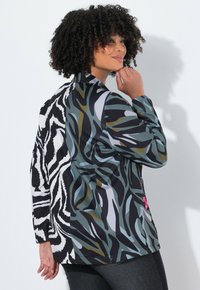 Giacca multicolore con design astratto di stampa animale; un lato presenta modelli verde scuro e nero, mentre l'altro lato ha strisce bold in bianco e nero.