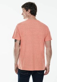 Pánské tričko s krátkým rukávem v korálově růžové barvě, vyrobené z měkkého materiálu s hladkou strukturou, s klasickým kulatým výstřihem a volným střihem.