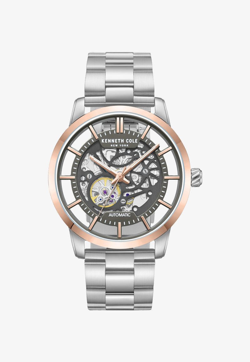 Silverfärgad rostfri klocka med en grå skelettskiva, rosaguld accenter och klara timmarkörer och visare. Automatisk rörelse synlig genom skivan.