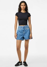 Piemērots melns īsām piedurknēm tops, augsta jostasvietas zila denima šorti ar priekšējām kabatām, gaiša mazgāšana un saplēsts apmale. Melni sporta apavi ar baltiem akcentiem.