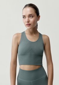 Mátově zelený sportovní crop top s těsným střihem, s texturovanou tkaninou a bezšvovým provedením v oblasti prsou a spodním lemu.