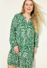 Robe verte avec un motif abstrait blanc, fermeture à boutons à l'avant, manches longues et ourlet volé. Tissu doux avec une coupe décontractée.