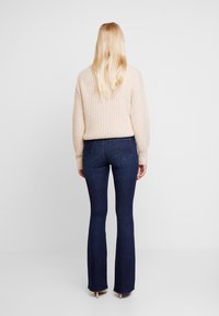 Beige ribbad tröja med avslappnad passform, som matchas med mörkblå utsvängda jeans. Outfiten ger en avslappnad look med en mjuk textur.