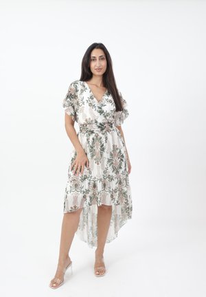Robe à imprimé floral avec un design enroulé, des manches courtes, un ourlet asymétrique et un fond blanc agrémenté de touches de vert et de rose. Sandales à talons transparent.