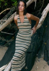 Hemdkragen, figurbetontes Kleid mit vertikalen Streifen in Schwarz, Creme und Beige. Stricktextur, mittellang, betont die Körperform.