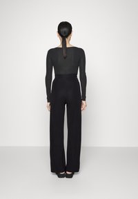 Černý top s dlouhými rukávy a širokými kalhotami. Hladká tkanina se přiléhavým pasem a uvolněným střihem. Jednoduchý design, minimální detaily a bez vzorů.