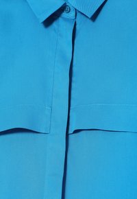 Light blue button-up shirt featuring a classic collar, smooth texture, and a front placket with two horizontal seams for design detail.