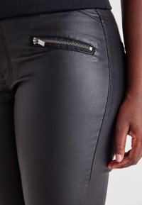 Black faux leather pants featuring a side zippered pocket, slim fit, smooth texture, and visible stitching details.