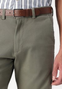 Pantalon vert en mélange de coton avec une texture lisse, doté d'une poche avant et d'une ceinture en cuir marron avec une boucle en métal argenté.