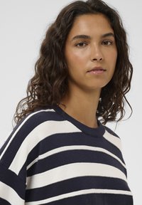 Gestreifter Pullover mit abwechselnden Streifen in Marineblau und Creme, weich gestrickte Textur, Rundhalsausschnitt und lässige Passform mit sichtbaren Nahtdetails.