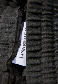 Donkergrijze stof met een geribbelde textuur, met een zichtbaar label met de tekst "LINDENBERG." De stof lijkt zacht en licht rekbaar.