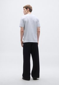 Helehall puuvillane lühikeste varrukatega t-särk, sobitatud tumedate laiade säärtega teksadega. Riietus on lõdva istuvusega ja minimalistliku disainiga.