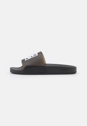 Sort slidesandal med bred rem med hvidt logo og tekstureret sål, set fra siden på en ensartet hvid baggrund.